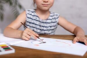 ispirato poco ragazza a il tavolo disegnare con vernici. avvicinamento foto