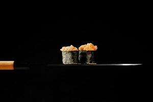 gunkan maki con guarnizione di crudo salmone e rosso tobiko su magro lama di giapponese coltello foto
