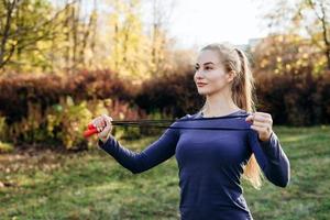 sorridente, bella ragazza bionda che fa saltare la corda all'aperto foto