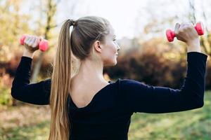 bella donna che lavora all'aperto. donna sportiva che si allena con manubri, vista posteriore foto