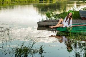 giovane donna con fiore ghirlanda su sua testa, rilassante su barca su fiume a tramonto. concetto di femmina bellezza, riposo nel il villaggio foto