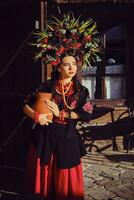 brunetta ragazza nel un' nero e rosso ucraino ricamato autentico nazionale costume e un' ghirlanda di fiori è in posa in piedi a il cancello. foto