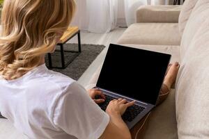 donna su divano Lavorando su il computer portatile con modello vuoto schermo. vuoto copia spazio su tenere sotto controllo per annuncio. nero schermo. foto