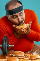 di mezza età uomo con barba, vestito nel un' rosso dolcevita, fascia per capelli, in posa con hamburger e francese patatine fritte. blu sfondo. avvicinamento. veloce cibo. foto