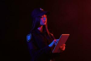 avvicinamento ritratto di un' femmina polizia ufficiale in posa per il telecamera contro un' nero sfondo con rosso e blu retroilluminazione. foto