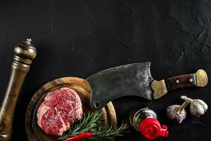 pezzo di Manzo filetto, con ascia per taglio e chopping carne, spezie erano cucinando - rosmarino, Pepe, sale, aglio. su vecchio di legno tavola su pietra nero tavolo. foto