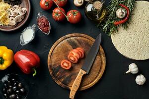 taglio di legno tavola con tradizionale Pizza preparazione ingredienti formaggio, pomodori, salsa, olive, oliva olio, Pepe, spezie. nero struttura tavolo sfondo foto