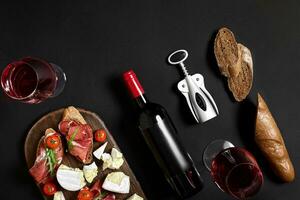 rosso vino, formaggio, ciliegia pomodoro, pane e prosciutto su di legno tavola al di sopra di nero sfondo, superiore Visualizza, copia spazio foto
