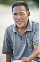 vicino su viso di asiatico anziano uomo con asciutto le foglie sigaretta guardare per telecamera foto