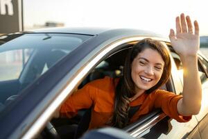 giovane donna guida auto e salutando. vicino su ritratto di giovane attività commerciale donna seduta nel il auto e ridendo mentre agitando foto