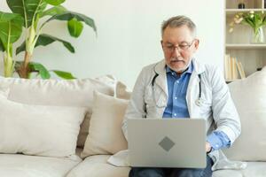 anziano uomo medico Lavorando con il computer portatile computer. professionale anziano maturo assistenza sanitaria esperto ricerca informazione o avere consultazione in linea nel ospedale camera. medicina assistenza sanitaria medico verifica. foto