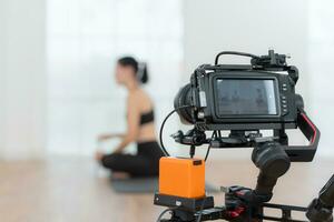 blogger registrazione vivere video lezione a casa. giovane donna seduta su yoga stuoia nel loto posizione e Tenere un' telecamera. foto