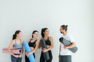 un' gruppo di femmina e maschio atleti si fermò e chiacchierato amichevolmente nel il studio prima inizio con il yoga classe. foto