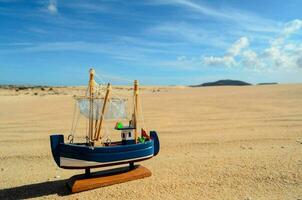 un' piccolo giocattolo barca si siede su il sabbia nel il deserto foto