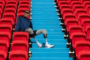 Disabilitato atleti nel un' blu camicia seduta su il rosso posti a sedere a il stadio, preparare per in esecuzione addestramento. foto