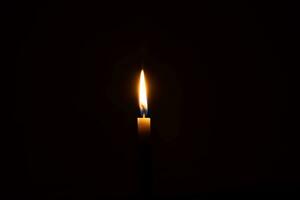 un' singolo ardente candela fiamma o leggero raggiante su piccolo arancia candela su nero o buio sfondo su tavolo nel Chiesa per Natale, funerale o memoriale servizio con copia spazio foto