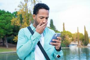 alunno guardare a il Telefono con un' sorpreso espressione all'aperto nel il città universitaria parco. foto