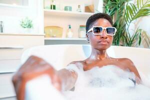 attraente africano donna nel vasca da bagno con occhiali da sole guardare a telecamera. foto