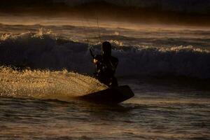 un' uomo aquilone imbarco nel il oceano a tramonto foto