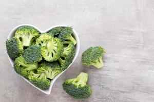 broccoli freschi in una ciotola a forma di cuore su uno sfondo di legno. foto