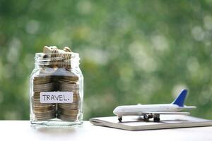 Salvataggio pianificazione per viaggio bilancio di vacanza concetto, finanziario, stack di monete i soldi nel il bicchiere bottiglia e aereo su passaporto con naturale verde sfondo foto