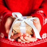 giovane donna di mani nel rosso Maglione Tenere regalo scatola con bianca nastro. avvicinamento. vacanza regalo. Natale, nuovo anno, San Valentino giorno e compleanno concetto. foto