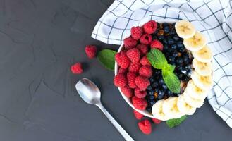 ciotola di muesli con fresco frutti di bosco e maturo Banana su un' buio sfondo. salutare prima colazione. copia spazio. foto