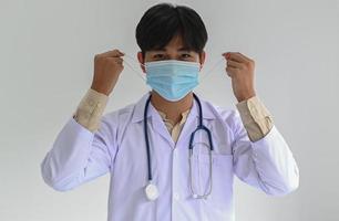 il professionista medico in un camice da laboratorio con uno stetoscopio indossa una maschera medica, foto frontale diritta.