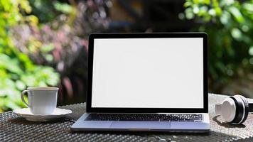 mockup laptop schermo vuoto e tazza da caffè con cuffie sul tavolo di ferro, sfondo albero verde. foto
