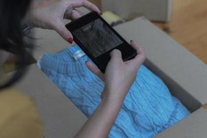 una donna che vende un prodotto online utilizza uno smartphone per scattare una foto del prodotto nella confezione.