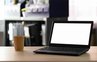 colpo ritagliato dello schermo vuoto del laptop con caffè da asporto sul tavolo in ufficio. foto