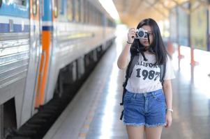 una donna adolescente che tiene una macchina fotografica su un binario del treno. foto