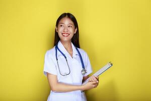 ritratto di un' bellissimo giovane donna nel un' giallo sfondo, asiatico donna indossare un' medico uniforme fa un' sorridente espressione, un' giovane donna indossare un' medico stetoscopio ha un' amichevole espressione. foto