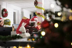 sorridente africano americano dipendente eccitato di regalo ricevuto a partire dal Santa Claus durante Natale vacanza stagione. lavoratore indossare travestimento sorprendente collaboratore con regali nel festivo decorato ufficio foto