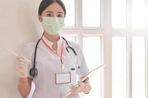 una dottoressa che indossa una maschera tiene in mano una cartella del paziente con uno stetoscopio. foto