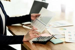 una donna d'affari in giacca e cravatta sta usando una calcolatrice e tiene in mano un grafico.
