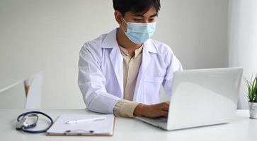 concetto medico, il medico che indossa un camice da laboratorio registra i risultati dell'auscultazione su un laptop.