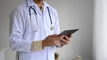 foto ritagliata di un medico in camice da laboratorio con uno stetoscopio che tiene in mano un tablet, vista laterale.
