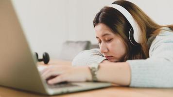 studentessa asiatica che dorme mentre studia online con laptop e cuffie.