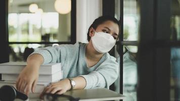 una studentessa asiatica che indossa una maschera medica si siede vicino alla finestra guardando fuori. foto