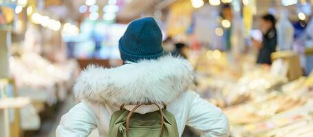 donna turista visitare nel hakodato, viaggiatore nel maglione giro turistico asaichi mattina mercato hakodate nel inverno. punto di riferimento e popolare per attrazioni nel hokkaido, Giappone. viaggio e vacanza concetto foto