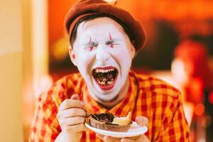 il clown è mangiare un' torta nel un' bar e il suo viso è gracchiare. foto