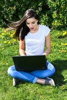 bellissimo ragazza seduta nel il parco con un' il computer portatile foto