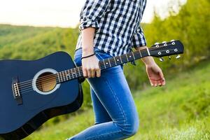 ragazza a piedi nel il campo con un' chitarra nel mano foto