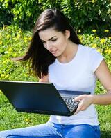 bellissimo ragazza seduta nel il parco con un' il computer portatile foto