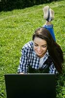 bellissimo ragazza seduta nel il parco con un' il computer portatile foto