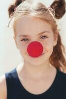 ritratto di un' poco ragazza con un' clown naso su il strada foto