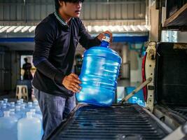 lavoratori sollevamento potabile acqua chiaro e pulito nel blu plastica gallone in il indietro di un' trasporto camion purificato potabile acqua dentro il produzione linea piccolo attività commerciale foto