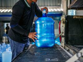 lavoratori sollevamento potabile acqua chiaro e pulito nel blu plastica gallone in il indietro di un' trasporto camion purificato potabile acqua dentro il produzione linea piccolo attività commerciale foto