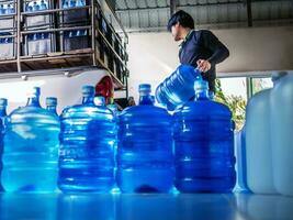 lavoratori sollevamento potabile acqua chiaro e pulito nel blu plastica gallone in il indietro di un' trasporto camion purificato potabile acqua dentro il produzione linea piccolo attività commerciale foto